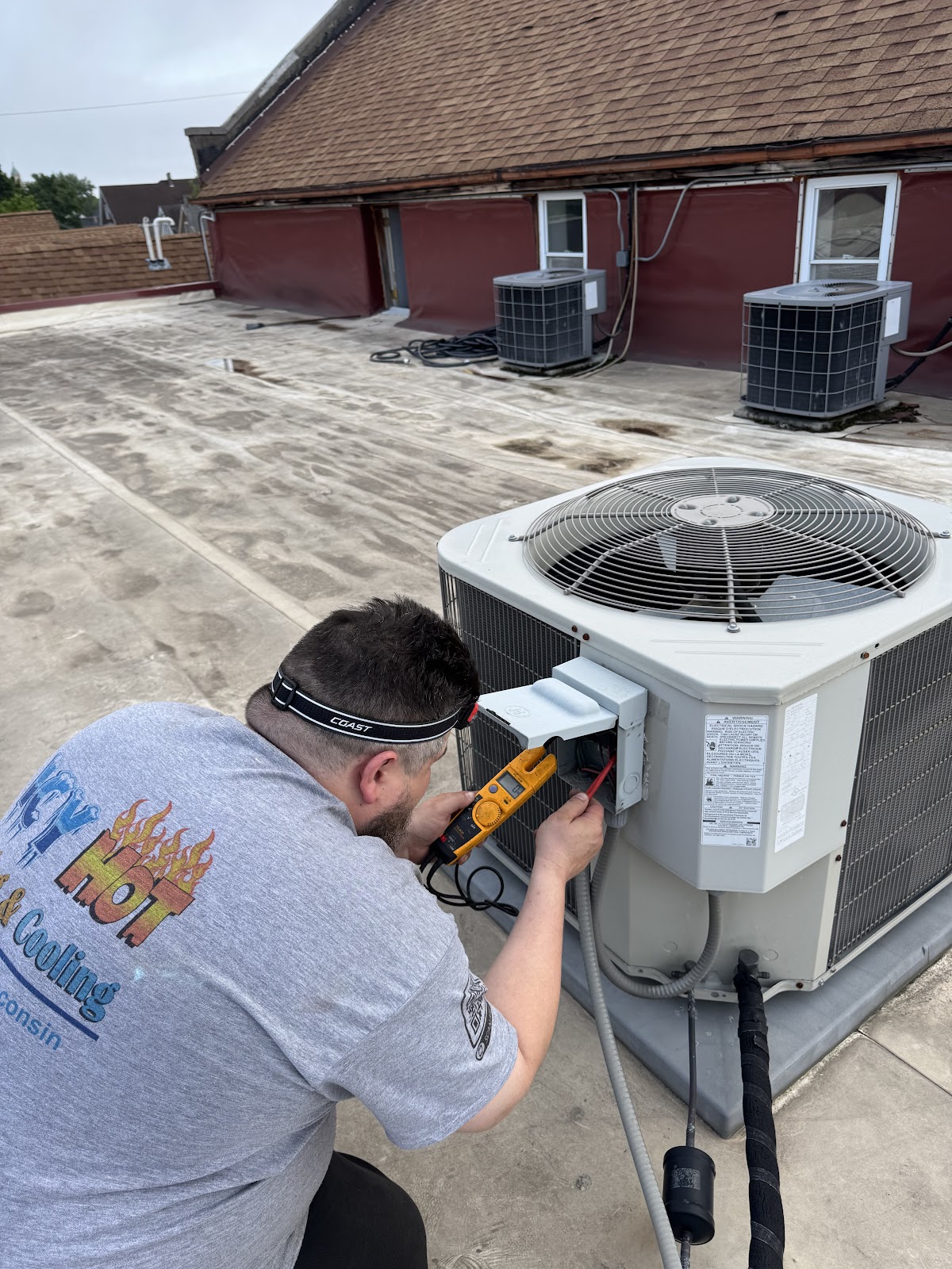 Icy Hot technician in a company shirt testing a rooftop condenser with a meter